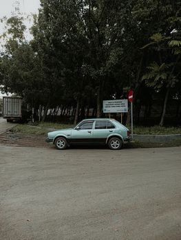 Classic hatchback car parked on a quiet street by a forested area.
