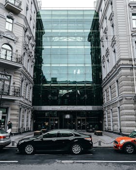 Glass facade building on a city street with parked cars and classic architecture.