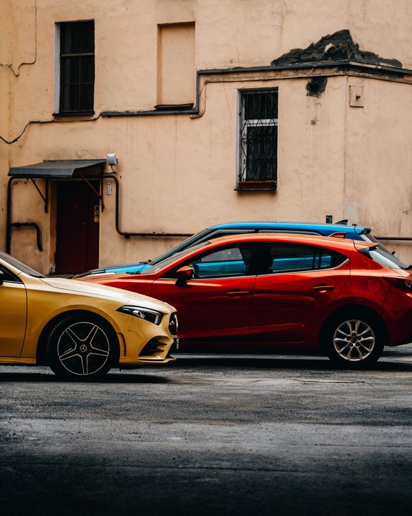 Carros amarelo e vermelho brilhantes estacionados ao longo de uma rua urbana em São Petersburgo.
