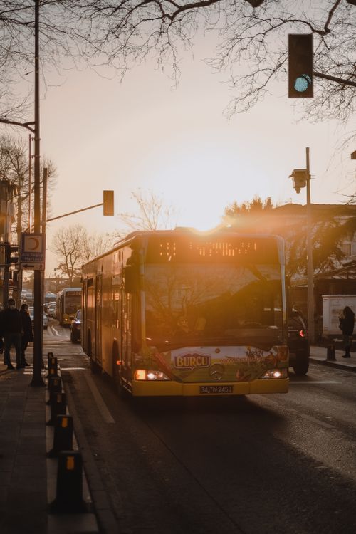 Free A city bus travels down a busy street at sunset, casting warm sun rays among leafless trees. Stock Photo