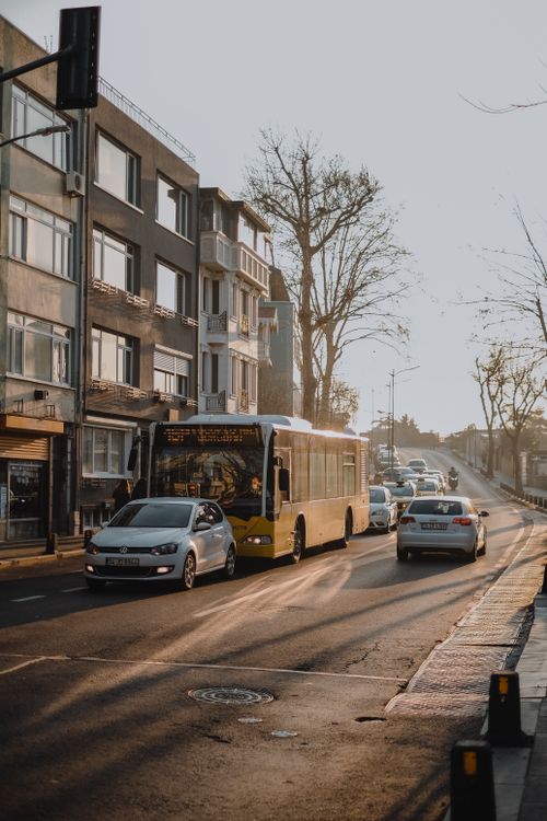 Free Passenger yellow bus driving on asphalt roadway with cars along residential building on sunny street with leafless trees in city Stock Photo