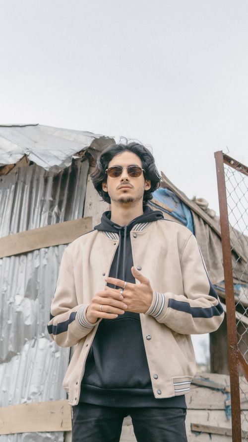Free Young man wearing sunglasses and a beige jacket posing outdoors against a rustic background in Fes, Morocco. Stock Photo