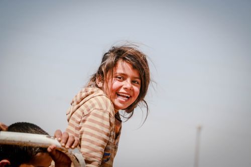 Free A young girl with a joyful expression smiling outdoors in Idlib, Syria under a clear sky. Stock Photo