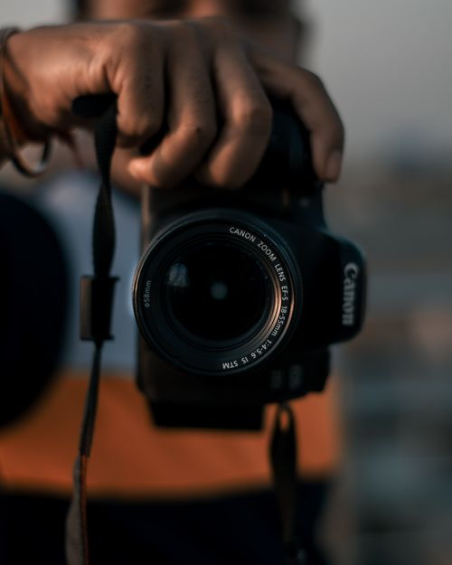 Free Close-up image of a person holding a DSLR camera outdoors in a casual setting. Stock Photo