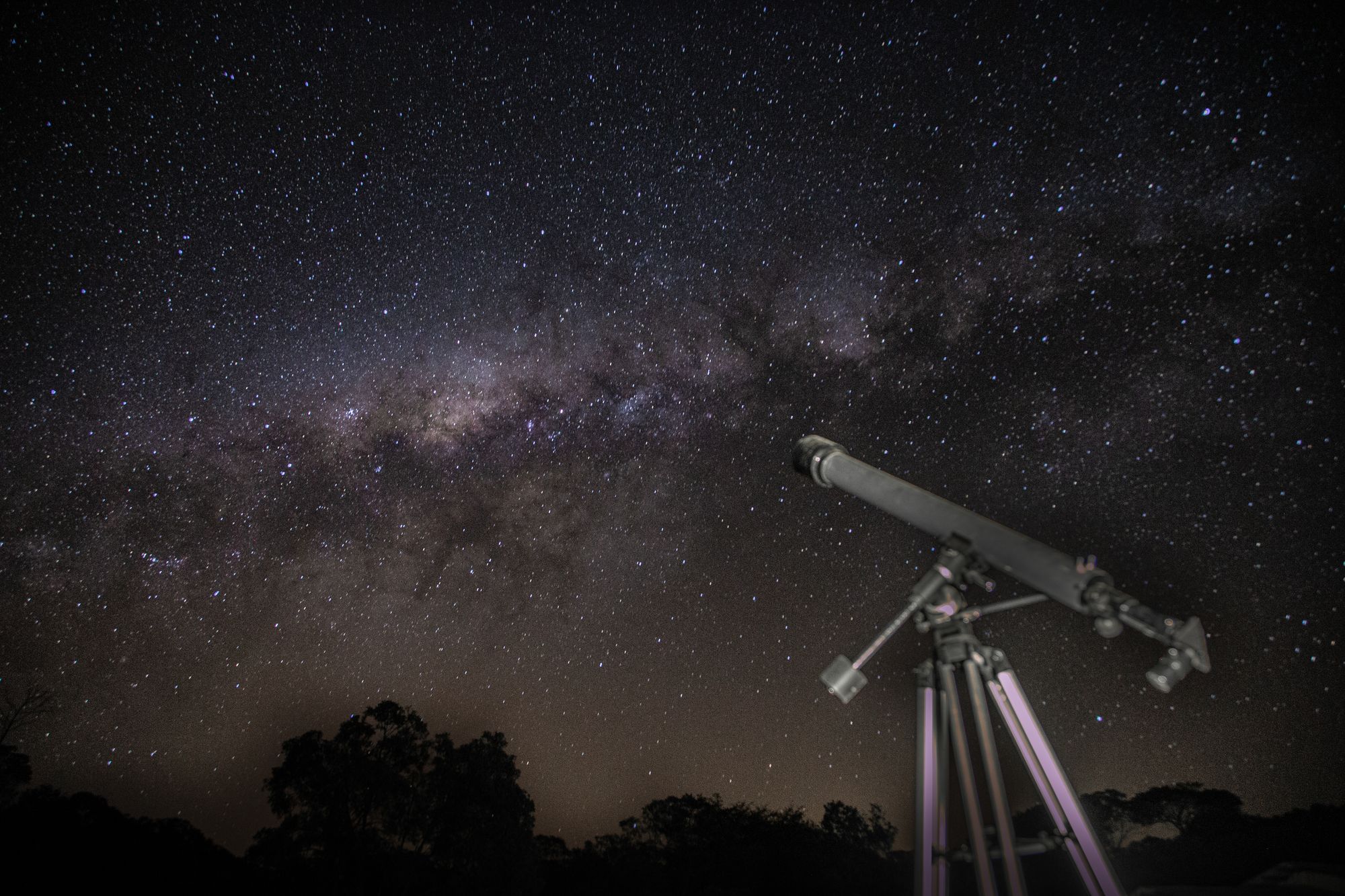 A telescope gazes at a stunning starry night sky showcasing the Milky Way.