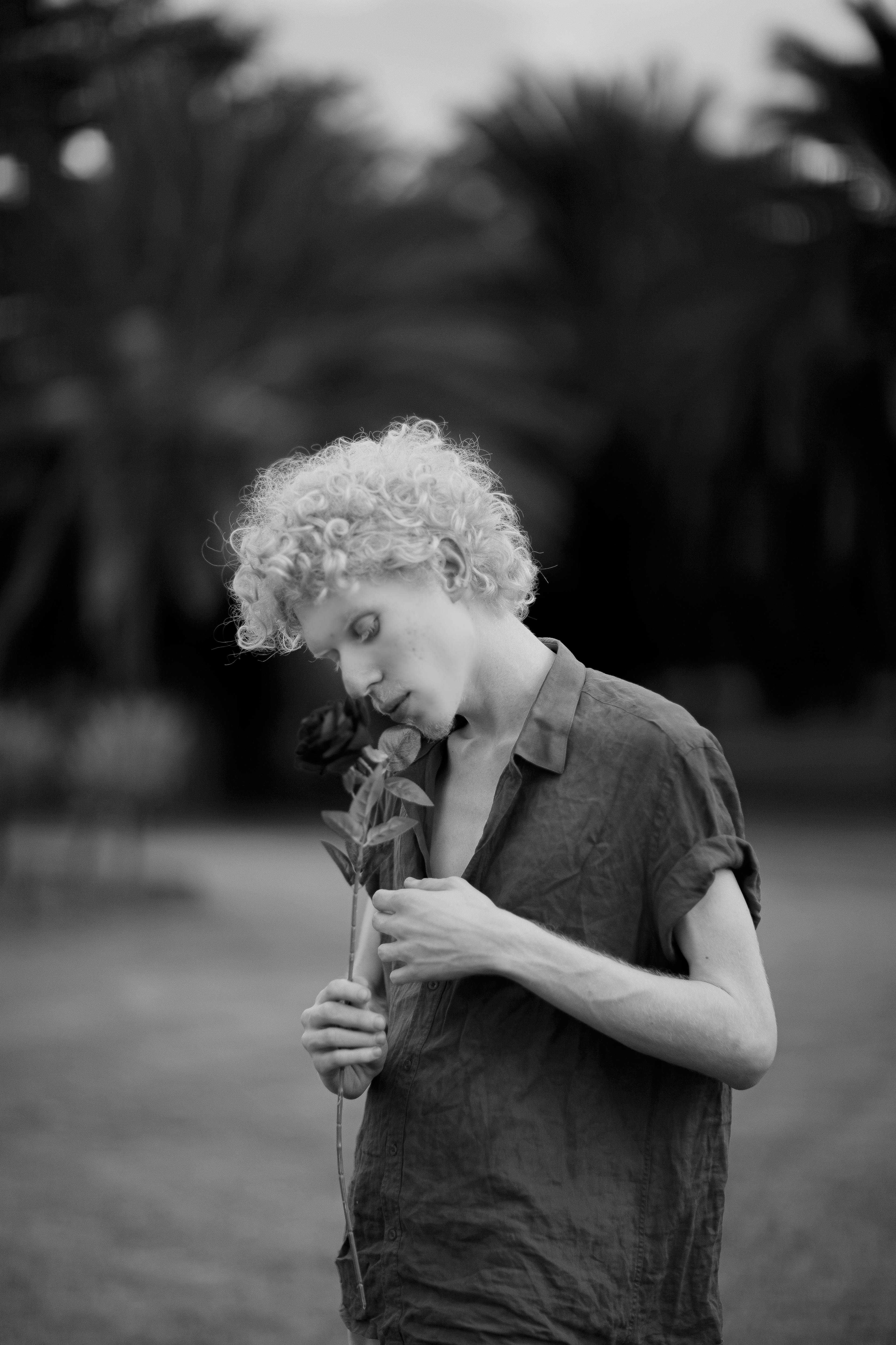 A man in a park holding a flower, captured in a serene black and white portrait.