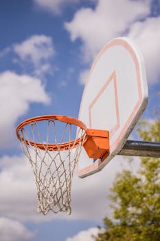 Low angle of basketball ring hanging on backboard against plants growing on sports court