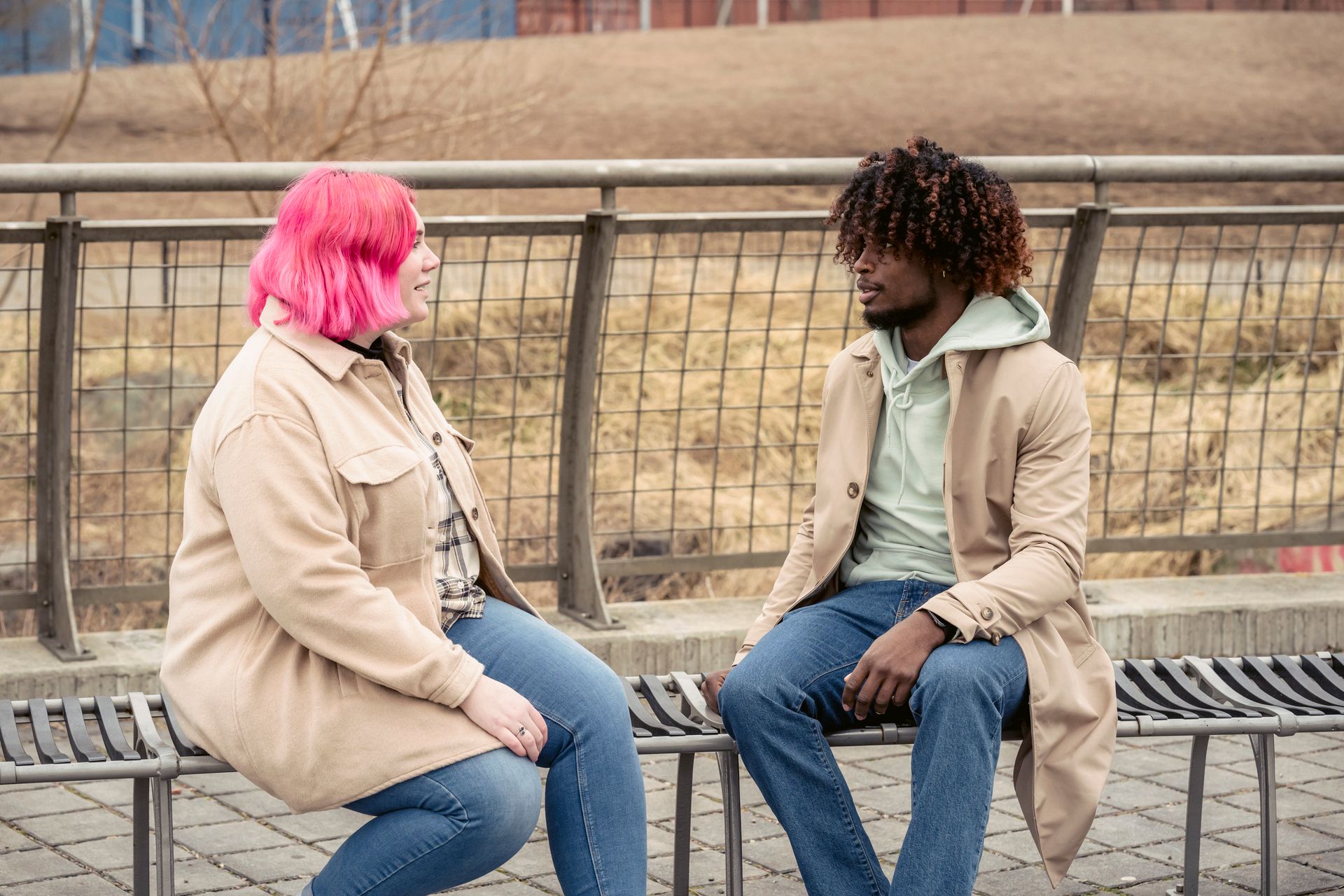Two people having a conversation on a bench outdoors in a park setting.