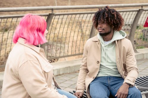 Free An interracial couple enjoys a casual conversation while sitting on a bench outdoors. Stock Photo