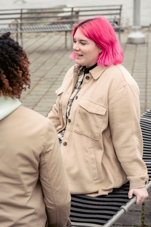 A Woman Wearing a Beige Coat Sitting on a Bench Beside a Person