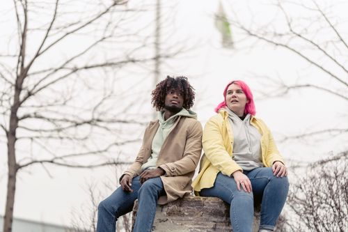 Free Two friends sitting on a rock outdoors, enjoying a cloudy day in casual attire. Stock Photo