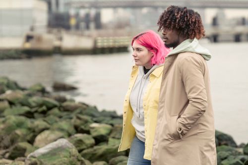 Free A couple walks along a rocky waterfront, embracing love and diversity. Stock Photo