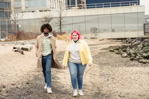 Free Full body of multiracial couple in jeans and outerwear strolling on embankment with stones against building during date in city Stock Photo
