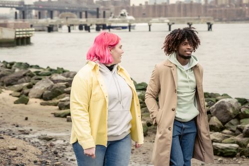 Free Content multiracial couple in outerwear strolling on embankment with stones near calm river against bridge and residential buildings in city Stock Photo