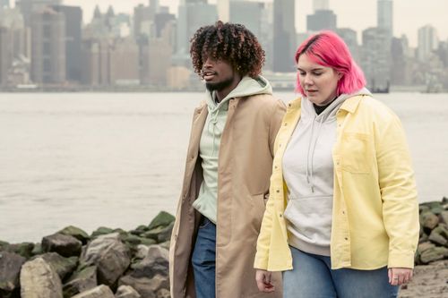 Free Multiracial couple in stylish clothes strolling on coast with stones near calm river against residential buildings during date in city Stock Photo