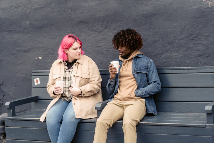 Friends Sitting On A Bench While Drinking Coffee