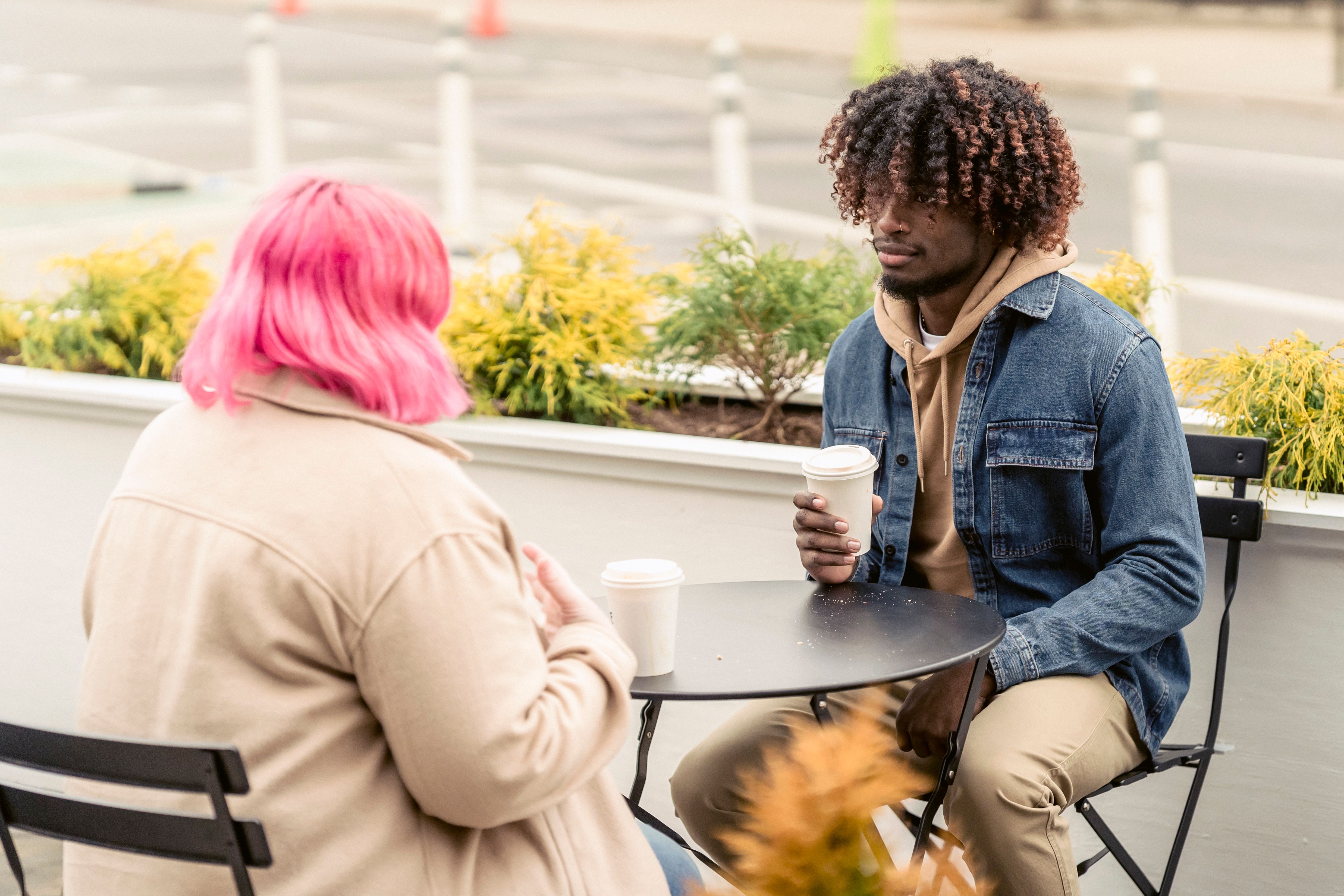 Two friends enjoying a casual coffee conversation outdoors at a cafe.