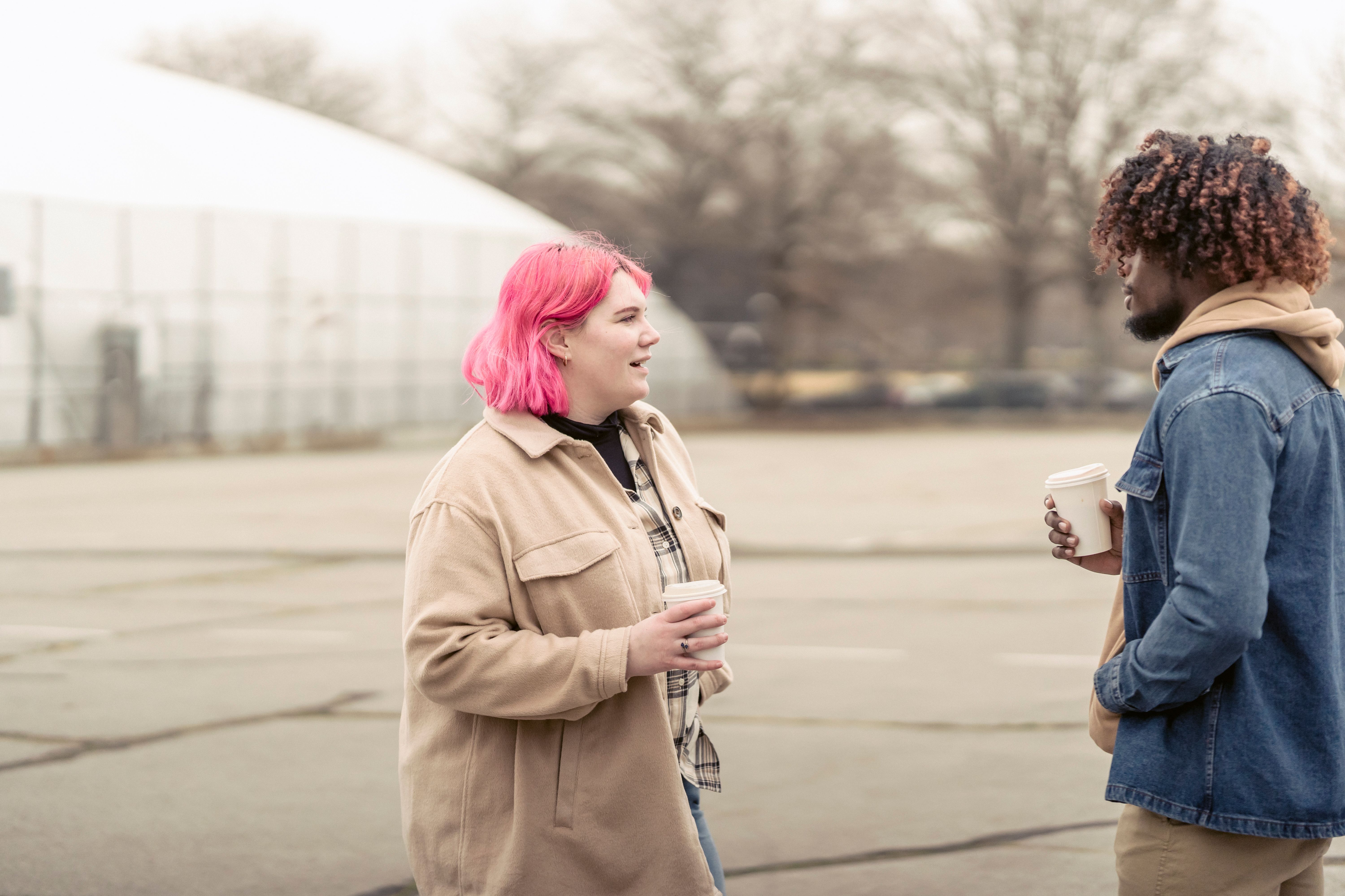 Two people talking on a city street, one holding a coffee cup