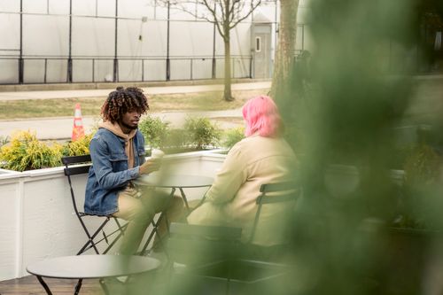Free Diverse man and woman sitting at table and talking on autumn day in street cafe Stock Photo