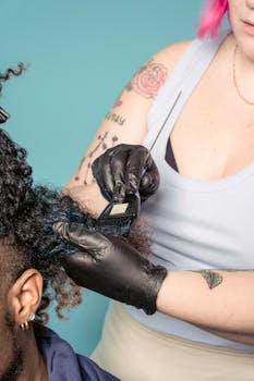 Unrecognizable woman in latex gloves applying dye on curly hair of man against blue background