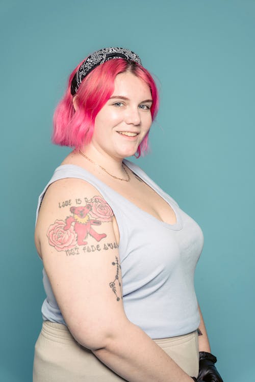 Free Side view of overweight smiling female with bright dyed hair and tattoos standing against blue background and looking at camera Stock Photo