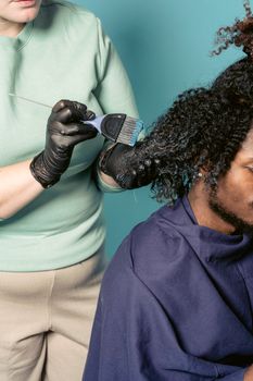 High angle of crop hairdresser in protective gloves dying curly hair of African American male customer in studio