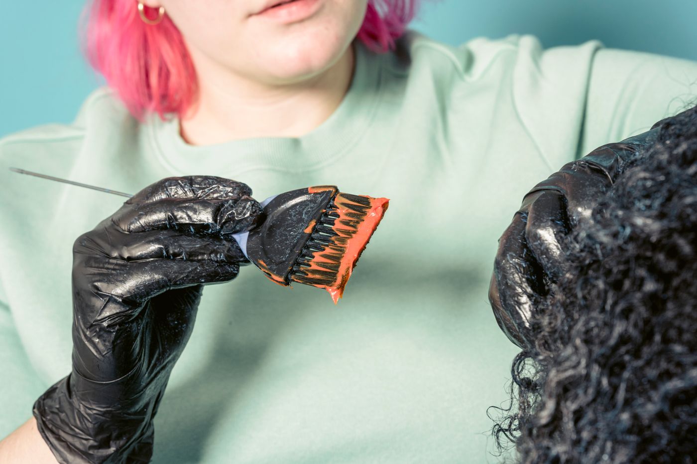 Hairdresser applying colour to a client's curly hair with a dye brush in a salon