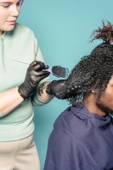 Professional hairdresser applies dye to client's curly hair in a studio setting.