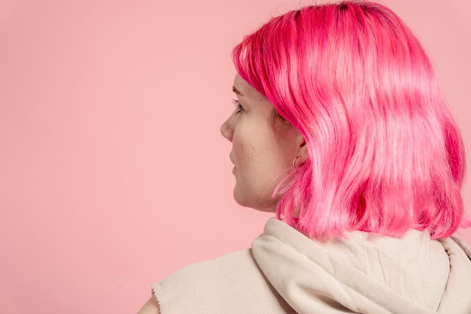 Back view of anonymous young female with dyed hair in casual outfit standing on pink background in modern light studio