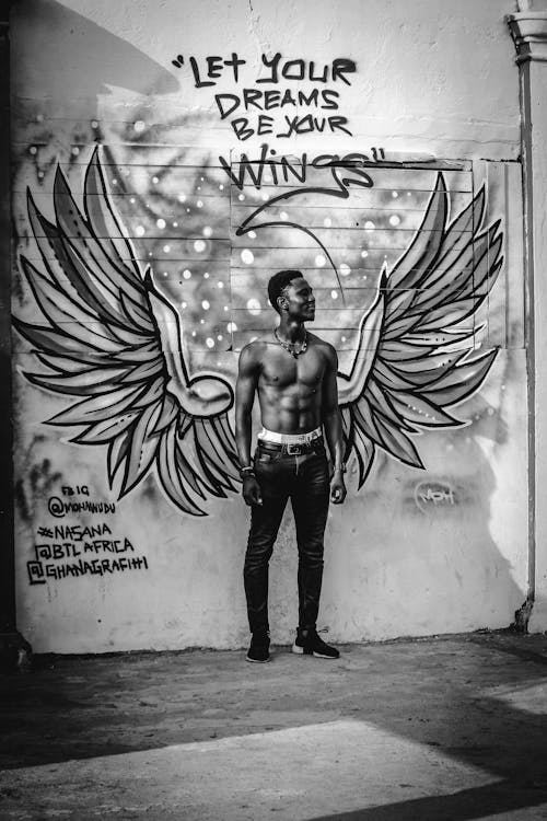 Man in Black Denim Jeans Standing Beside Graffiti Wall
