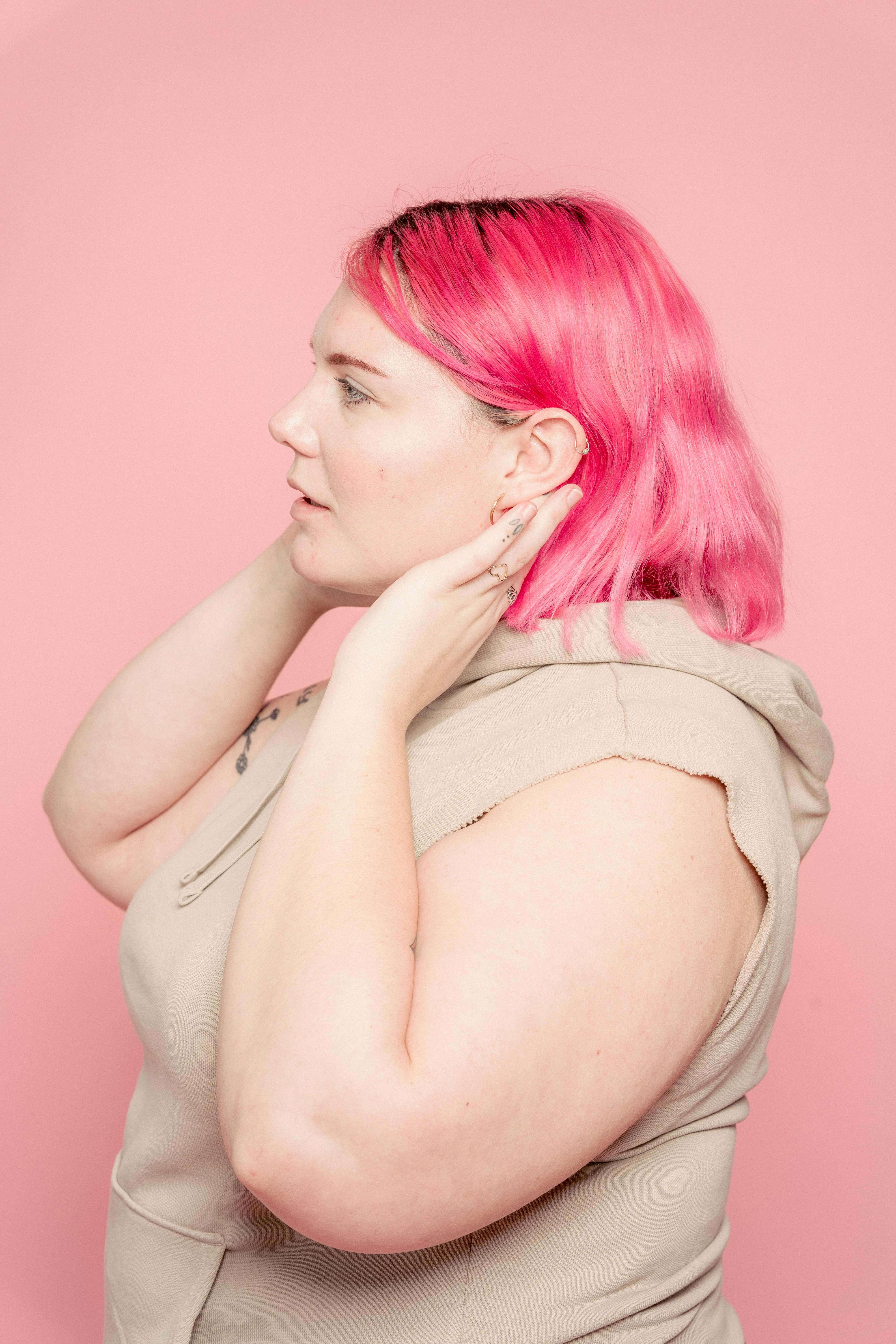 Side view of plus size female with dyed hair wearing casual wear standing on pink background in modern light studio