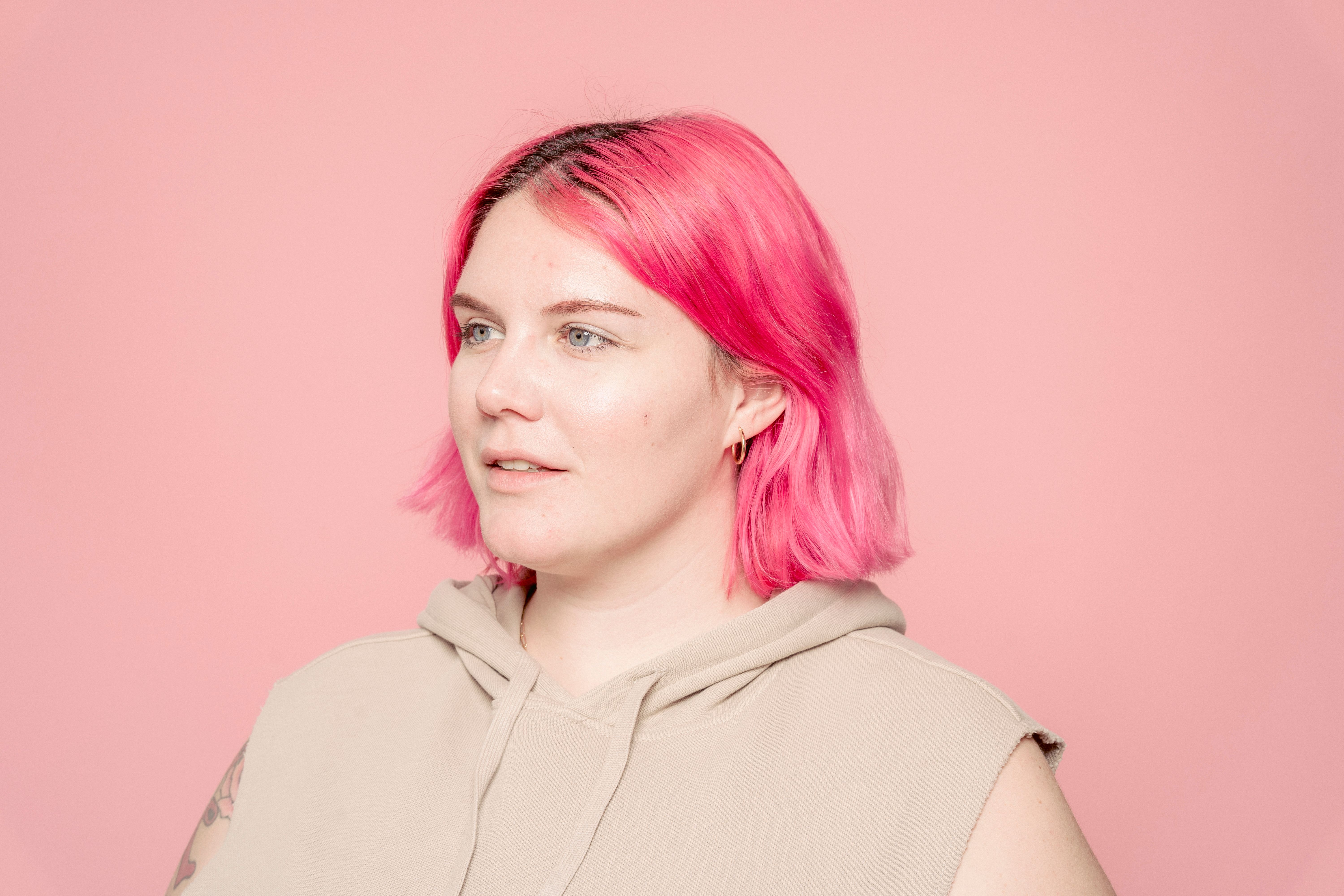 Young female model with dyed bright hair wearing casual sleeveless shirt and looking away against pink background