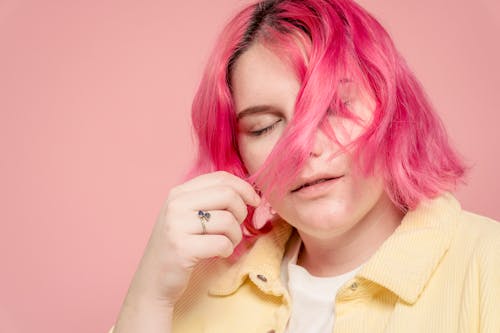 Female model with dyed hairstyle covering face with hair and closing eyes against pink background