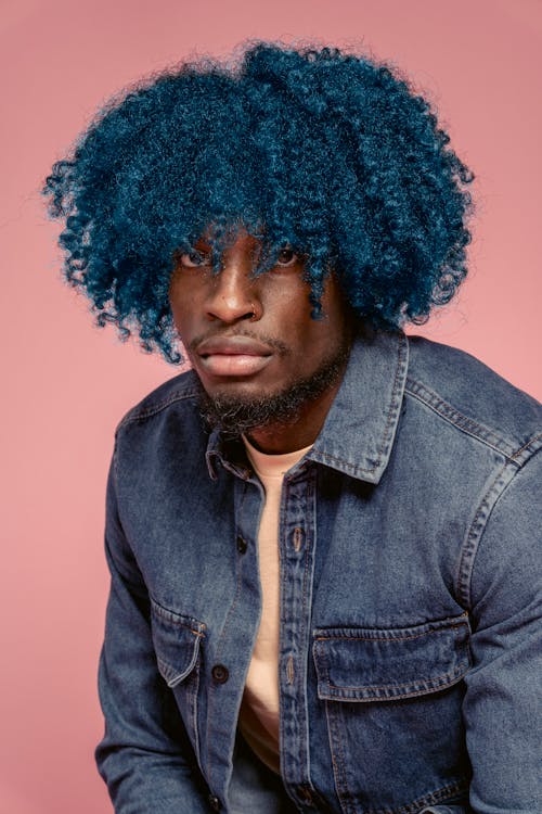 Confident African American male with blue dyed hair wearing casual denim jacket and t shirt looking at camera