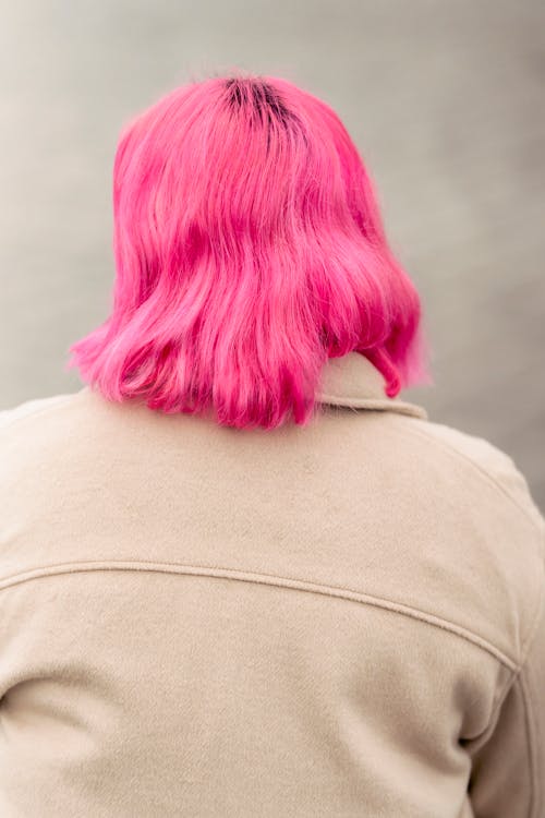 Back view of unrecognizable female with dyed pink hair sitting on shore of pond in solitude