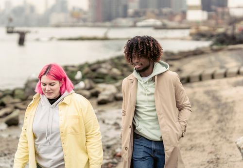 Free Content woman with dyed hair and African American man in outerwear strolling together on waterfront near river in city against residential buildings Stock Photo