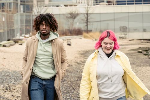 Free Positive woman with pink hair and African American man in outerwear strolling on street with buildings while spending in city Stock Photo