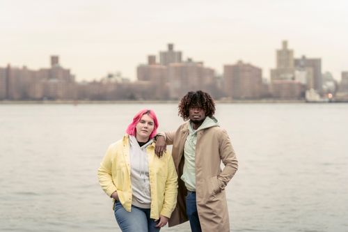 Free Cool African American man and woman with pink dyed hair warm clothes standing close together on river bank on blurred background of city Stock Photo