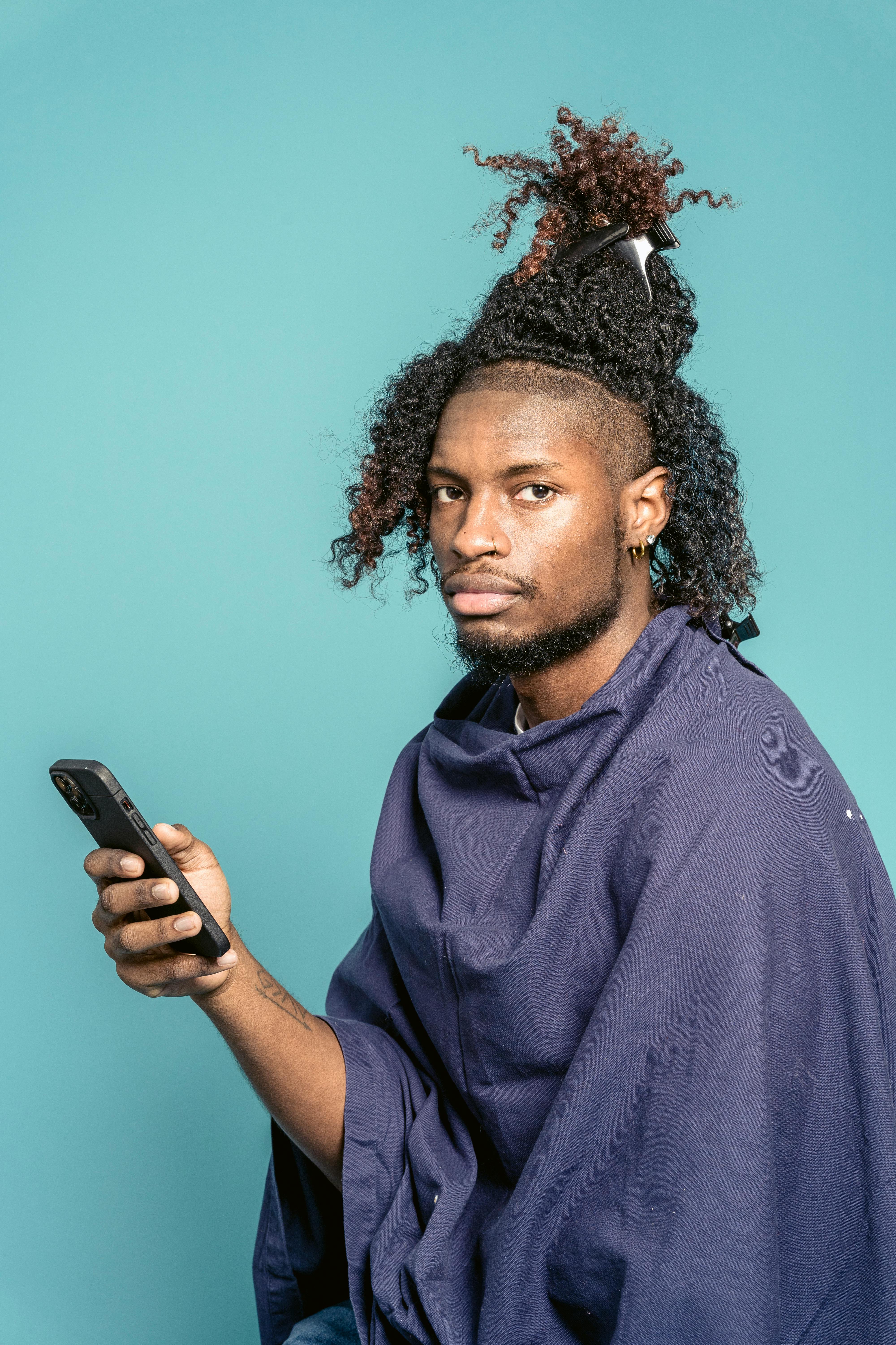 african american man in barber cloak using smartphone