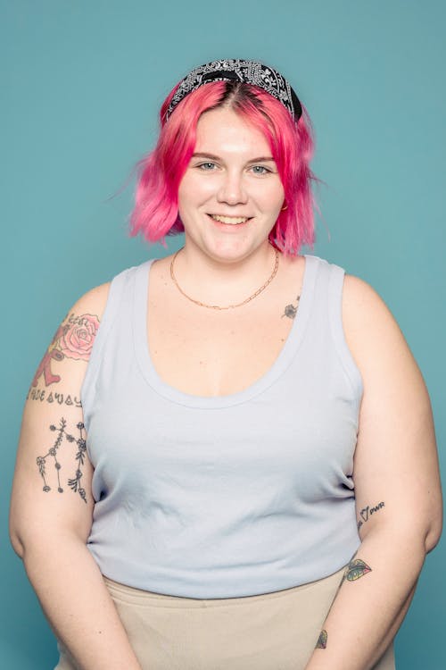 Smiling female with brightly dyed hair and tattooed arms looking at camera against blue background