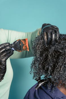Close-up of hairstylist applying hair dye on client with curly hair in salon.