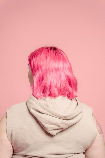 Back view of anonymous plus size female with dyed hair and tattoos on hands against pink background