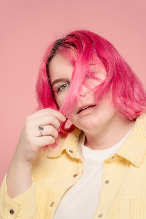 Free Young female with blue eyes covering face with dyed hair and opening mouth against pink background Stock Photo