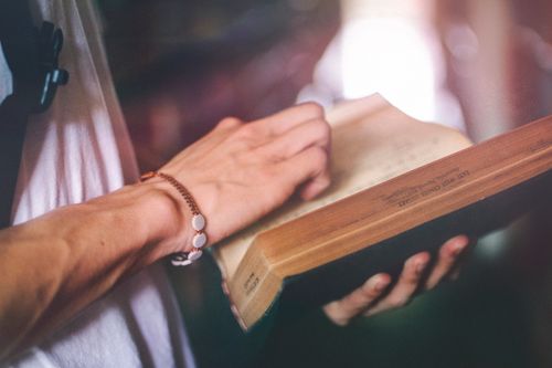 Free A person wearing a bracelet is reading an open book in a softly lit setting. Stock Photo
