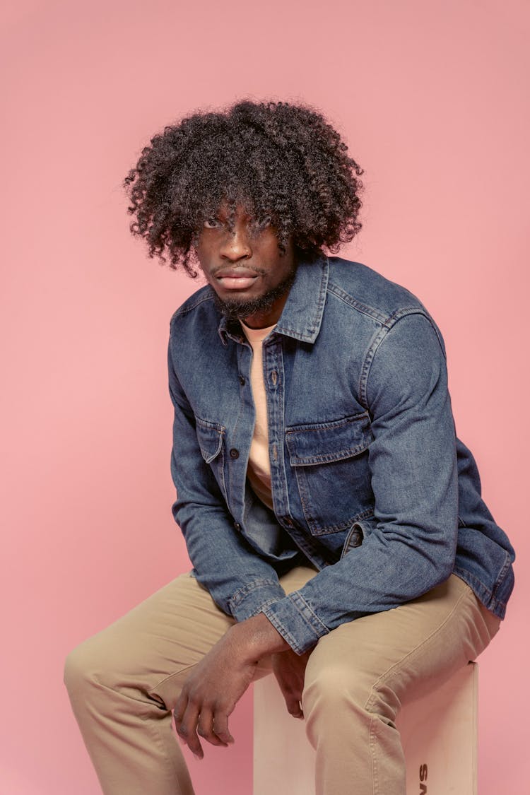 Serious Black Man In Casual Outfit Sitting On Pedestal