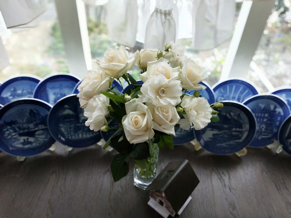 Free White Rose Flowers in a Vase Besides Ceramic Plates Stock Photo