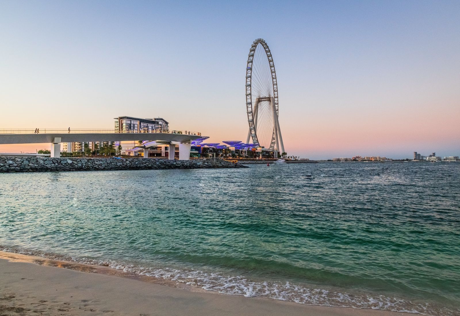 Ain Dubai wheel and the Bluewaters bridge at dusk, seen from the beach across the water