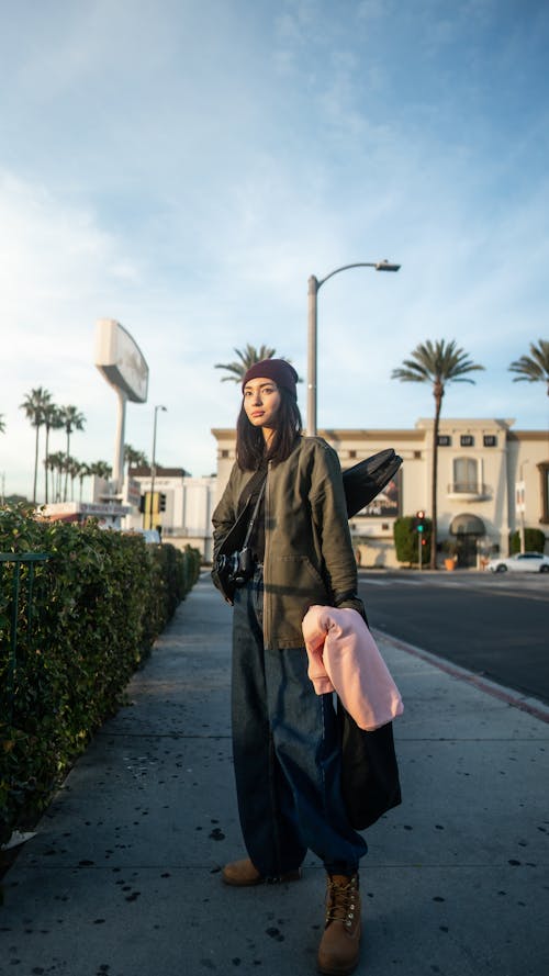 Trendy female with ukulele in case standing on sidewalk in city