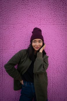 Cheerful young woman in trendy clothes standing with hand on waist and looking away against bright pink wall