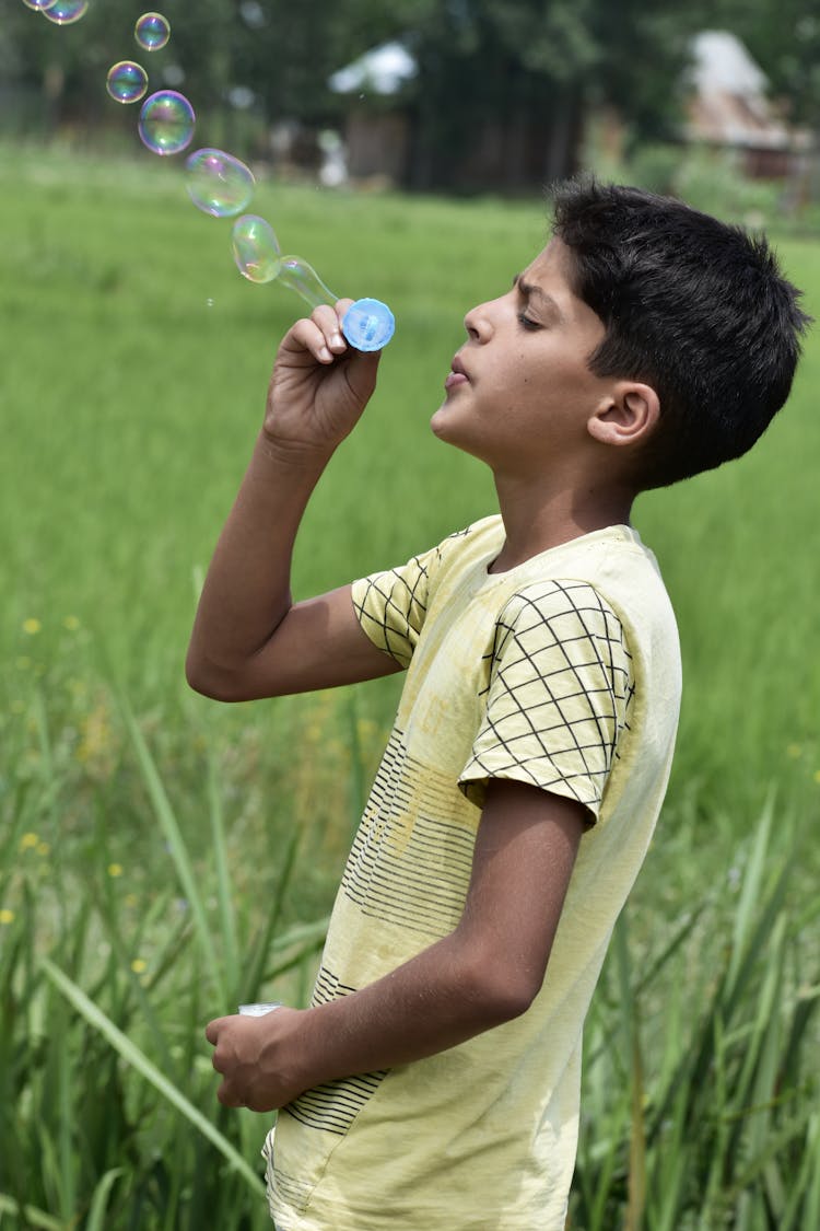 A Boy Blowing Bubbles On Green Grass